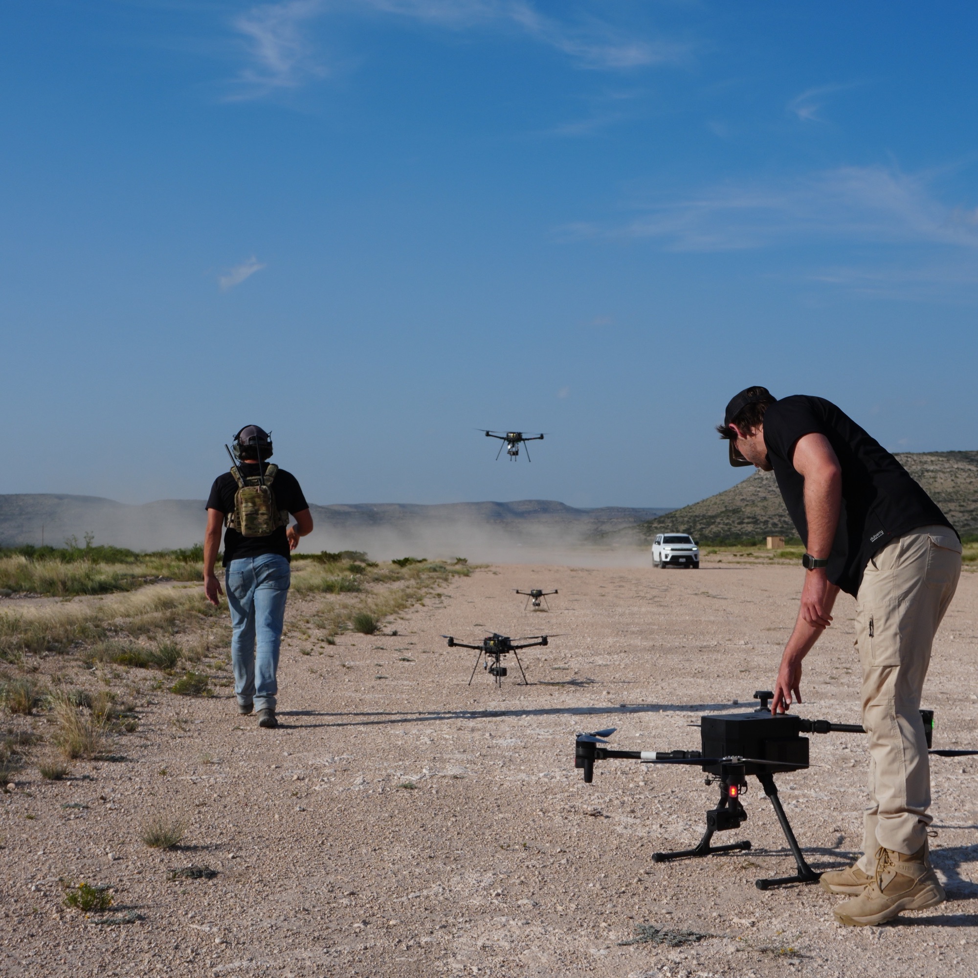 Two colleagues on a desert range launching a group of quadcopters.