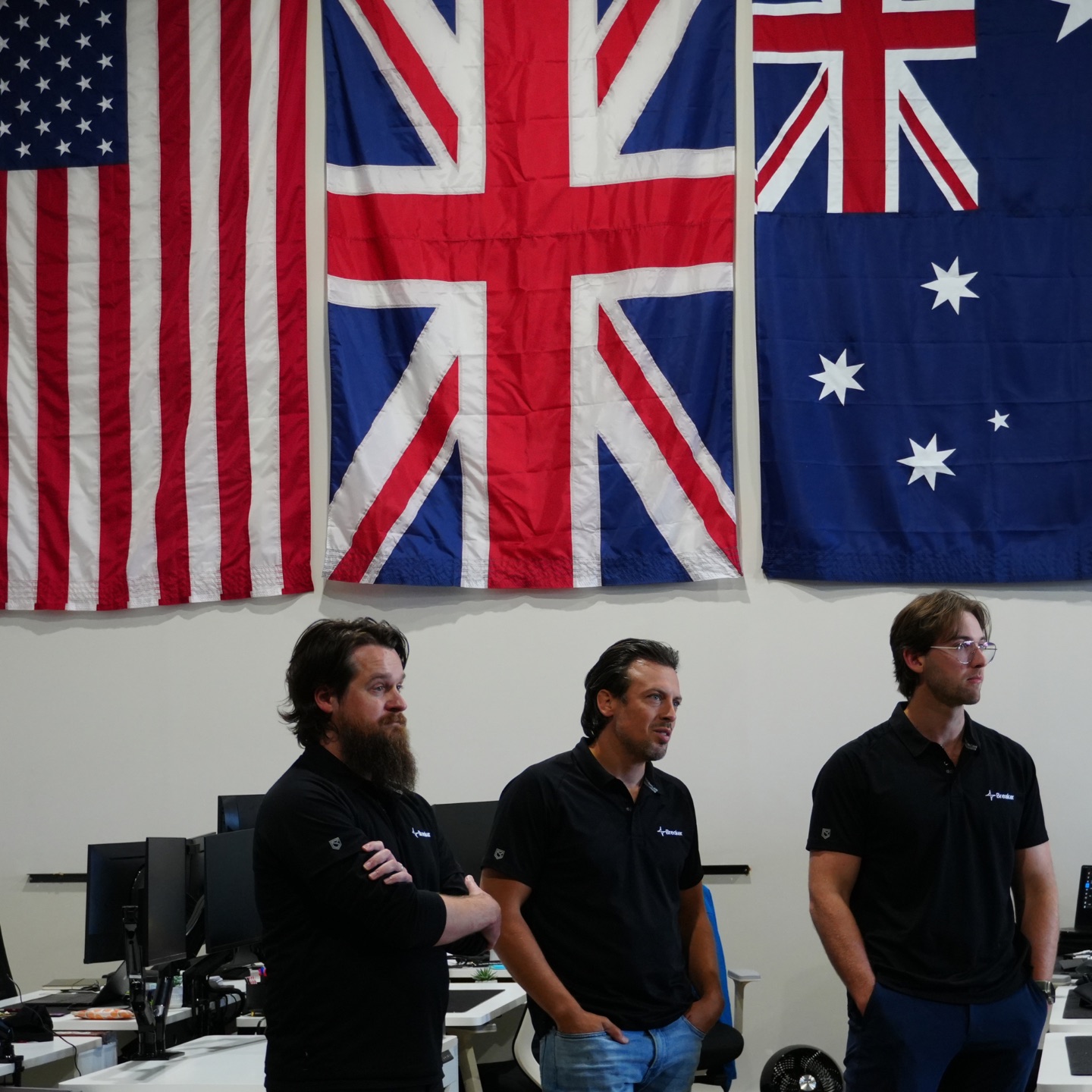 Three colleagues in the workshop, beneath the US, UK and Australian flags.