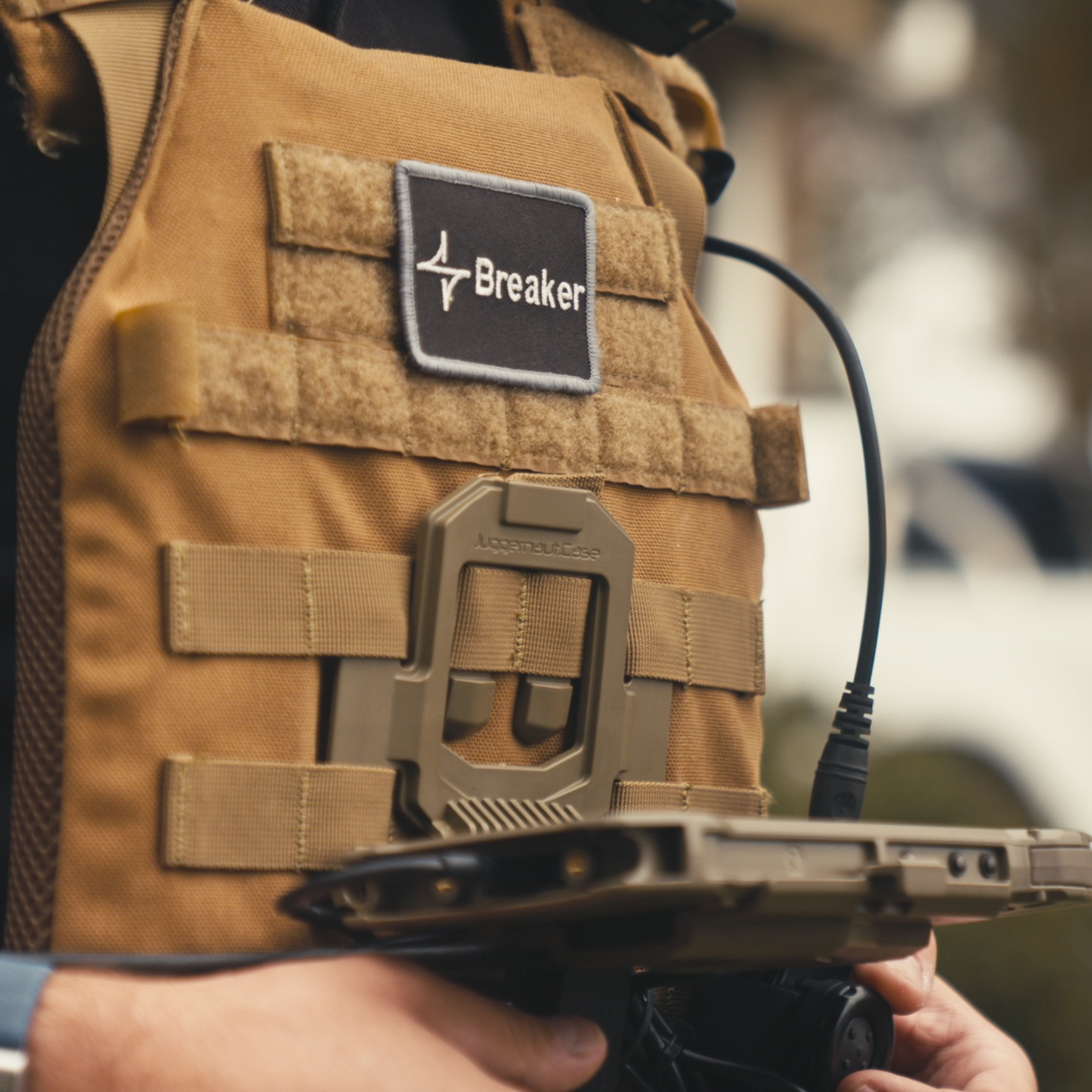 A plate carrier with a Breaker patch, hands on a rugged tablet.