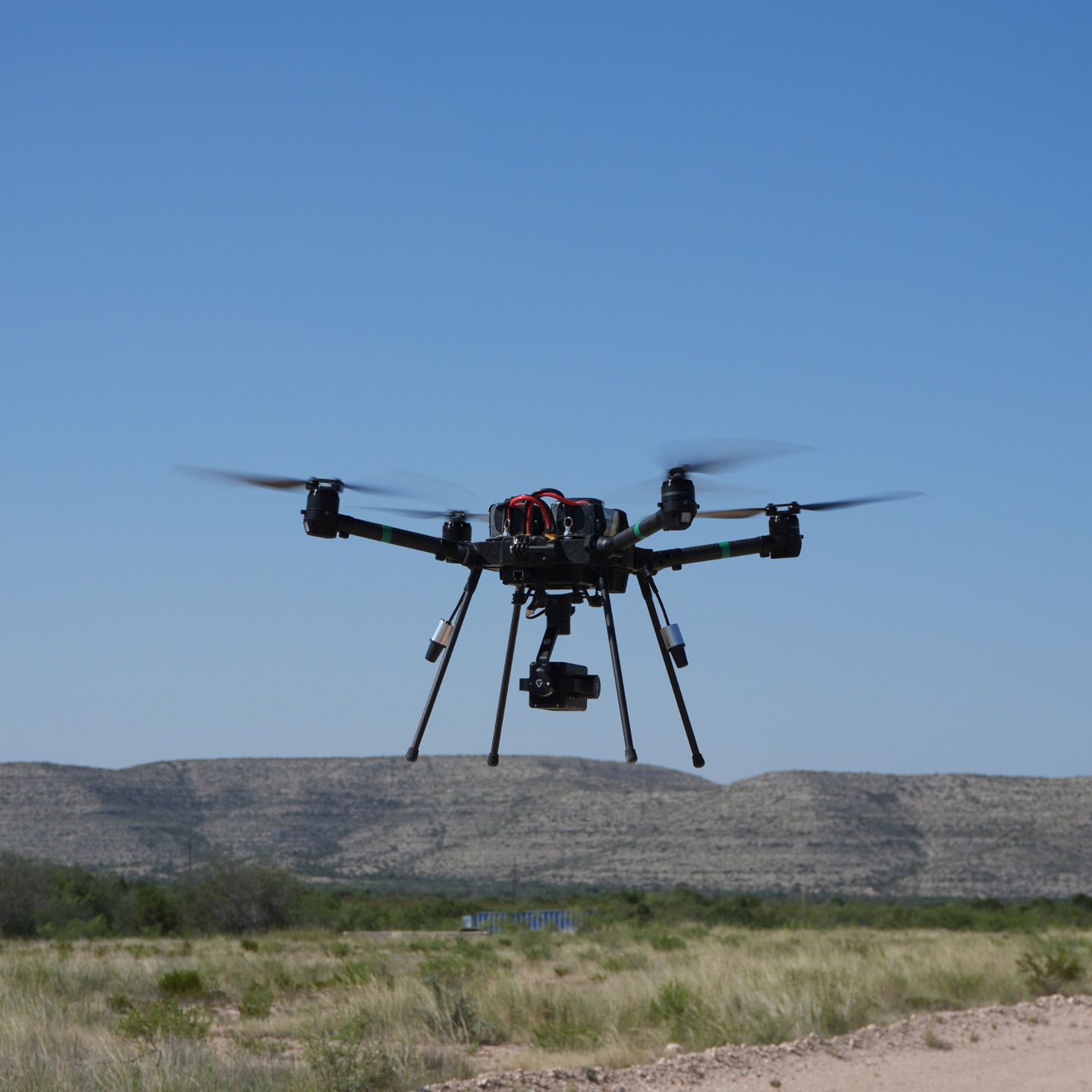 A quadcopter in flight over open scrubland.