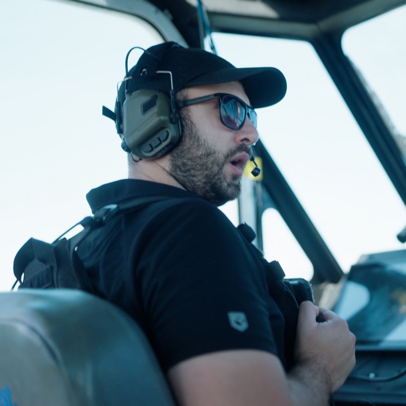 An operator at the wheel in a headset, watching the ground ahead.