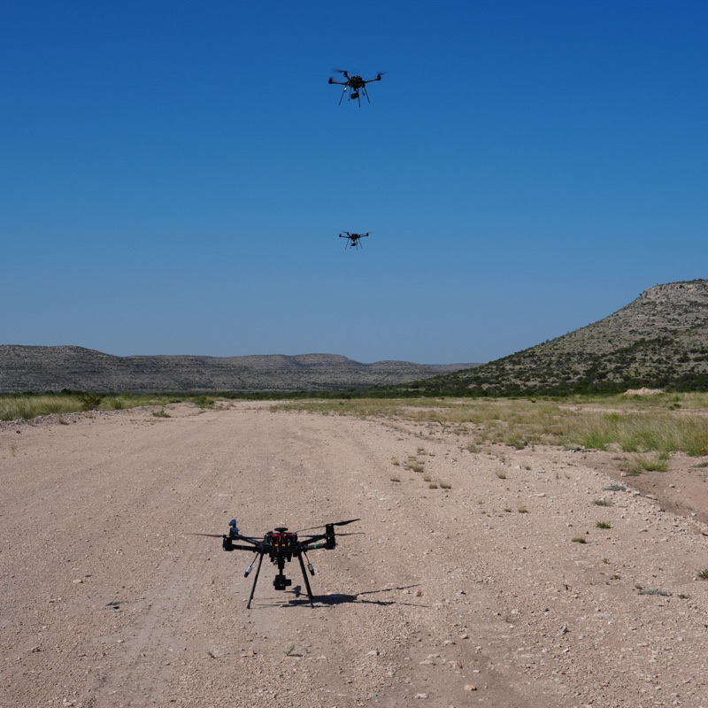Three quadcopters, two airborne and one on the ground.
