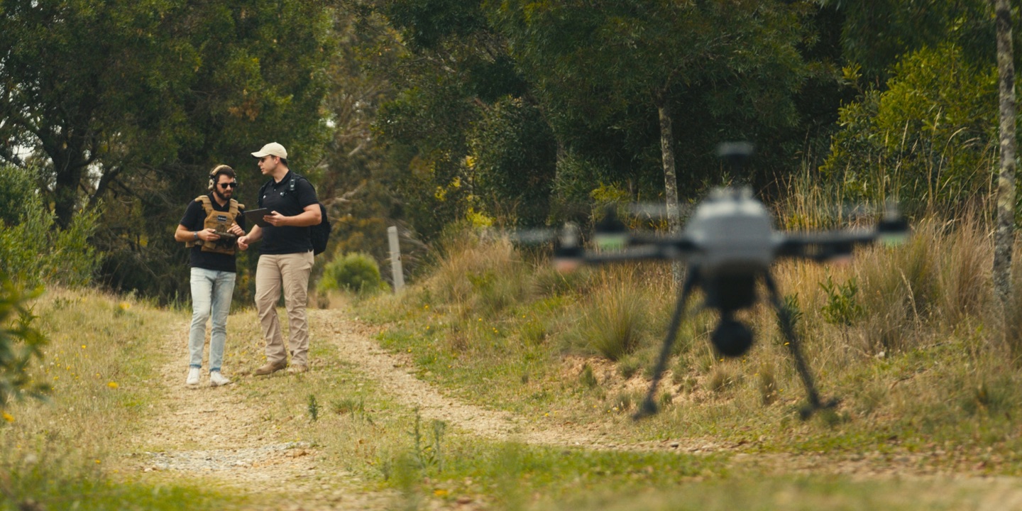 Two colleagues on a track walking a quadcopter out to its launch point.