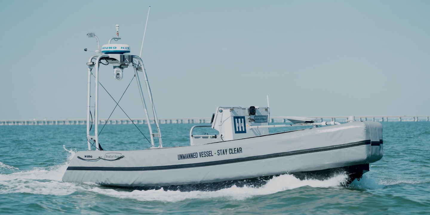 An uncrewed surface vessel under way, its hull marked UNMANNED VESSEL - STAY CLEAR.
