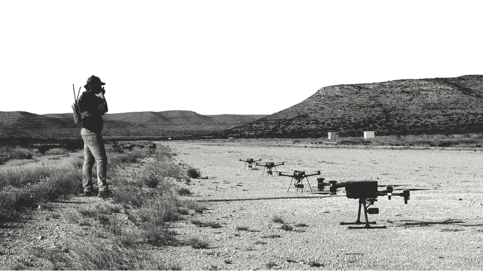 An operator speaks into a radio as a line of drones waits on a desert airstrip.