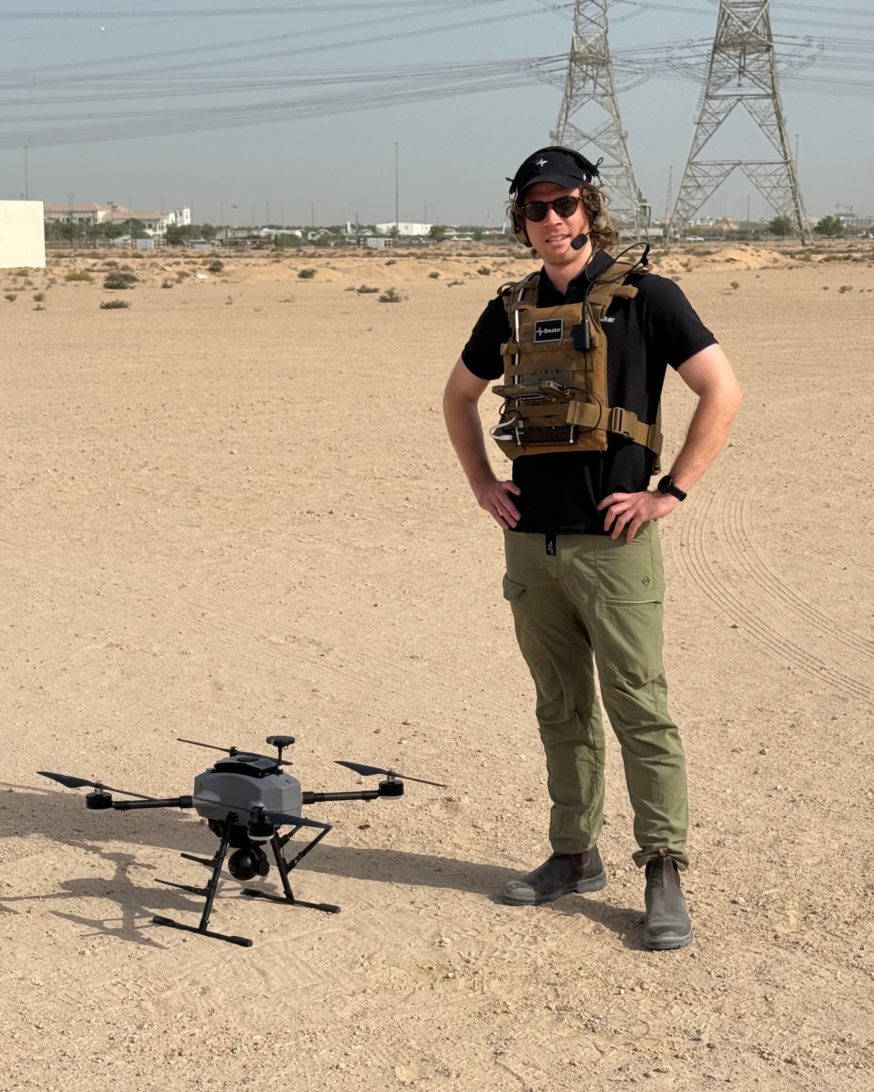 Jack Scott standing beside a quadcopter on a desert range.