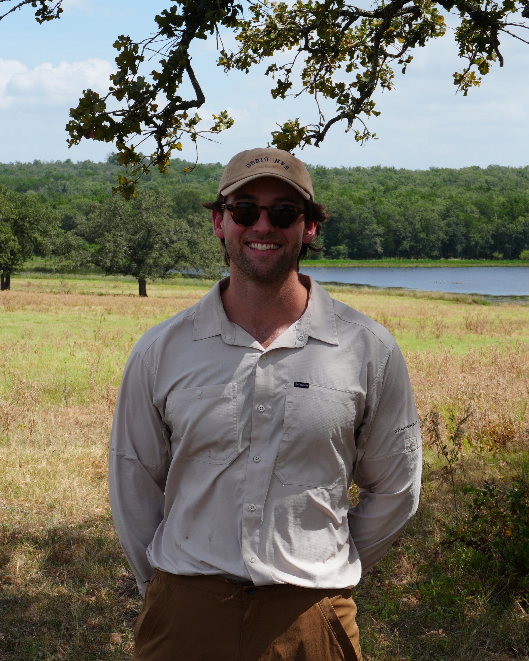 Khan Schroder-Turner standing in a field under an oak, a lake behind him.