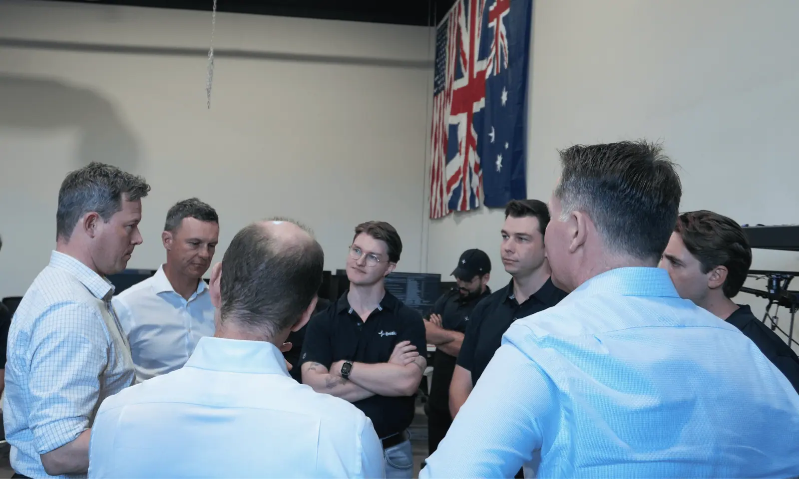 Members of the Australian Army delegation in discussion with Breaker engineers beneath the US, UK and Australian flags.