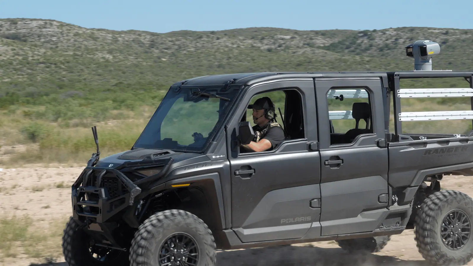 A Breaker operator driving a Polaris Ranger fitted with a gimbal camera, speaking into a headset.