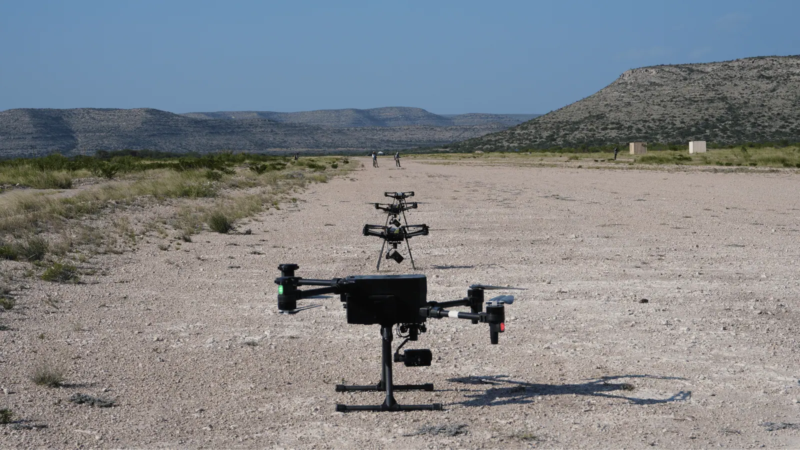 Three Breaker quadcopters lined up on a dirt airstrip on a range, with hills behind.