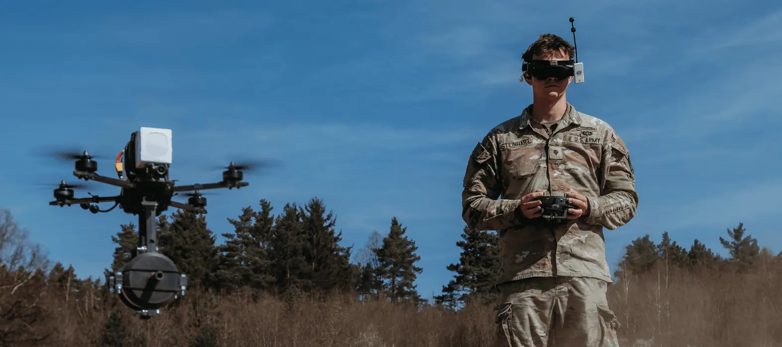 An operator flying a drone with a hand controller in open ground.