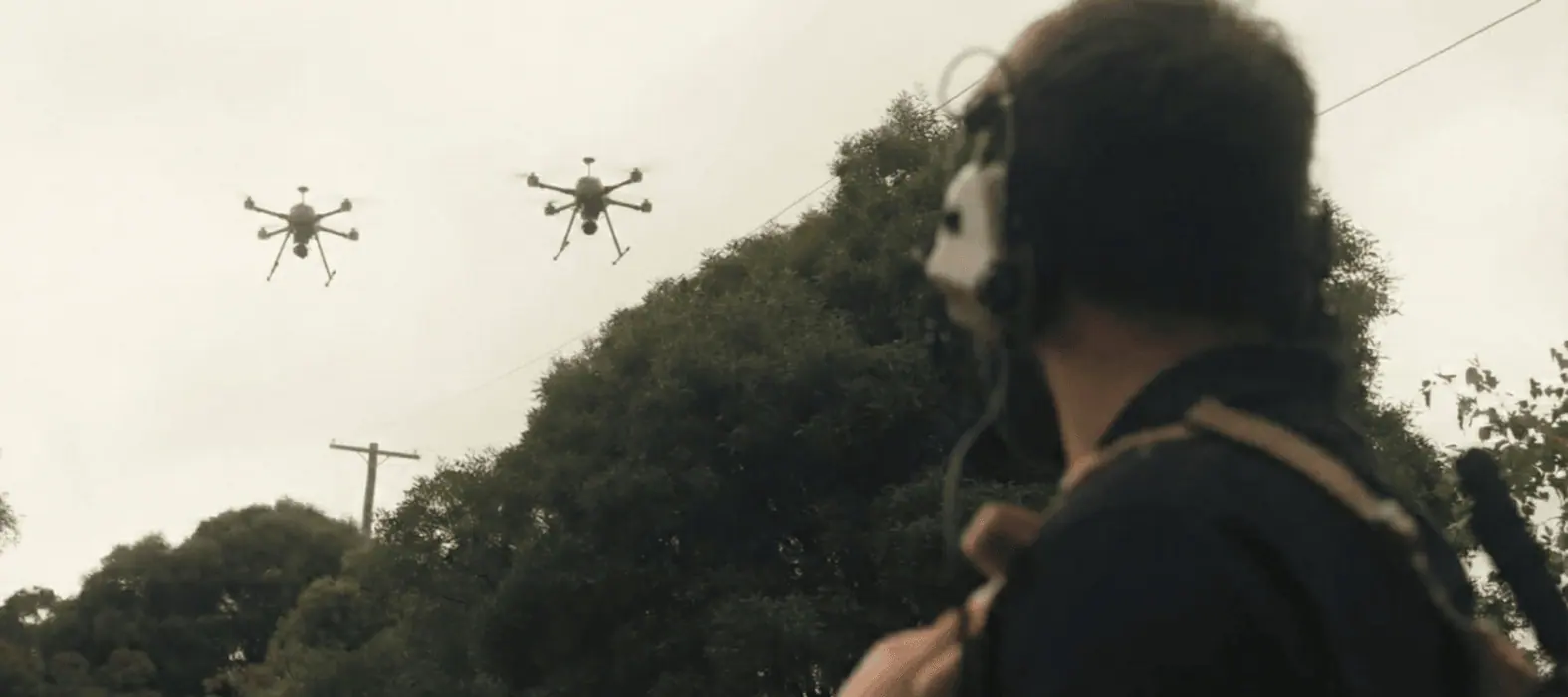 An operator with a headset watching two drones overhead.